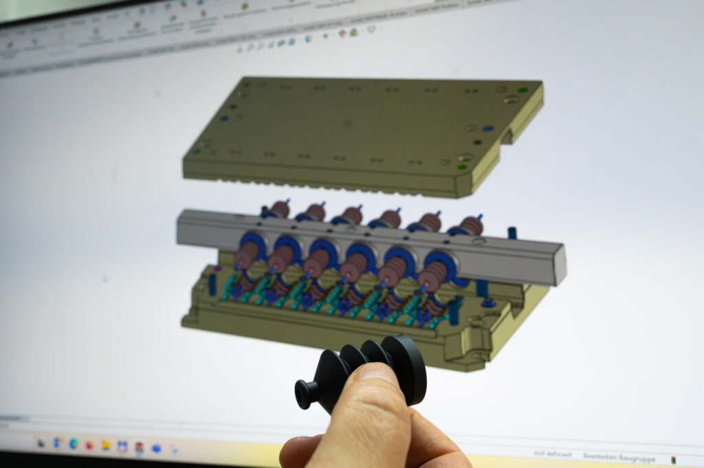 Azubi vergleicht Gummiformteil mit CAD Grafik am Computermonitor