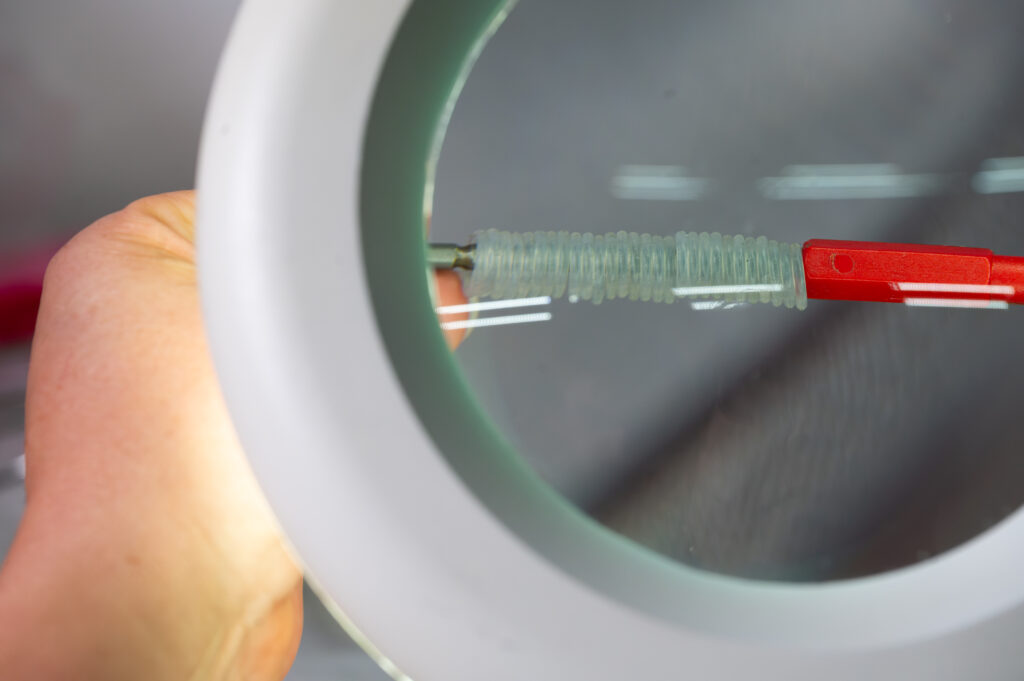 Unter einer Lupe werden kleine durchsichtige Silikonringe auf eine Stange gestapelt